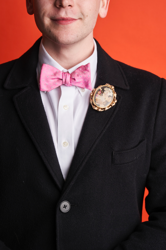 man in blue suit and pink bowtie wearing a decorative oval brooch