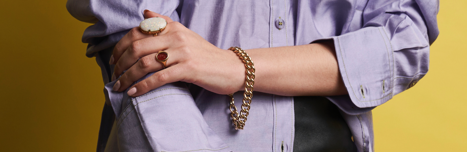 a woman in a purple shirt wearing rings and a bracelet on a gold background
