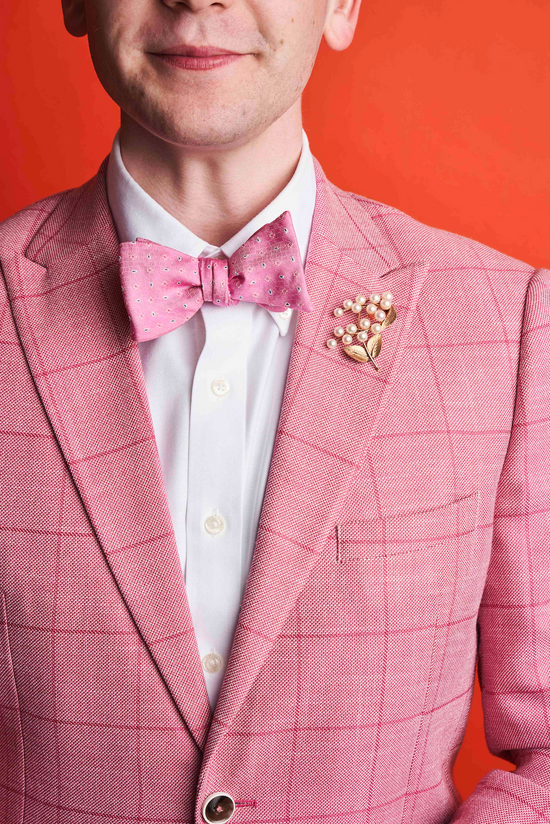  man in pink suit and bowtie wearing a pearl brooch